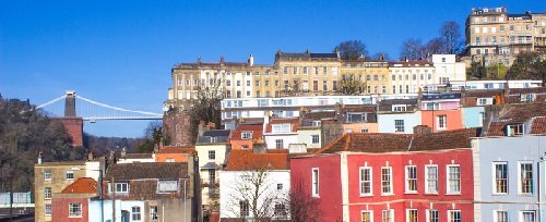 An image of the colourful houses that line the river Avon in Bristol, with the Clifton Suspension Bridge in the background